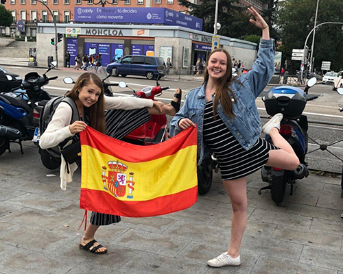 Mia und ihre Freundin halten eine spanische Flagge und machen dabei akrobatische Verränkungen